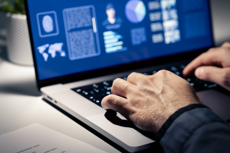 Close-up of a person typing on a laptop displaying charts and maps, suggesting cyber analysis or data investigation in a dimly lit workspace, possibly researching PeopleSearchNow Opt Out options.