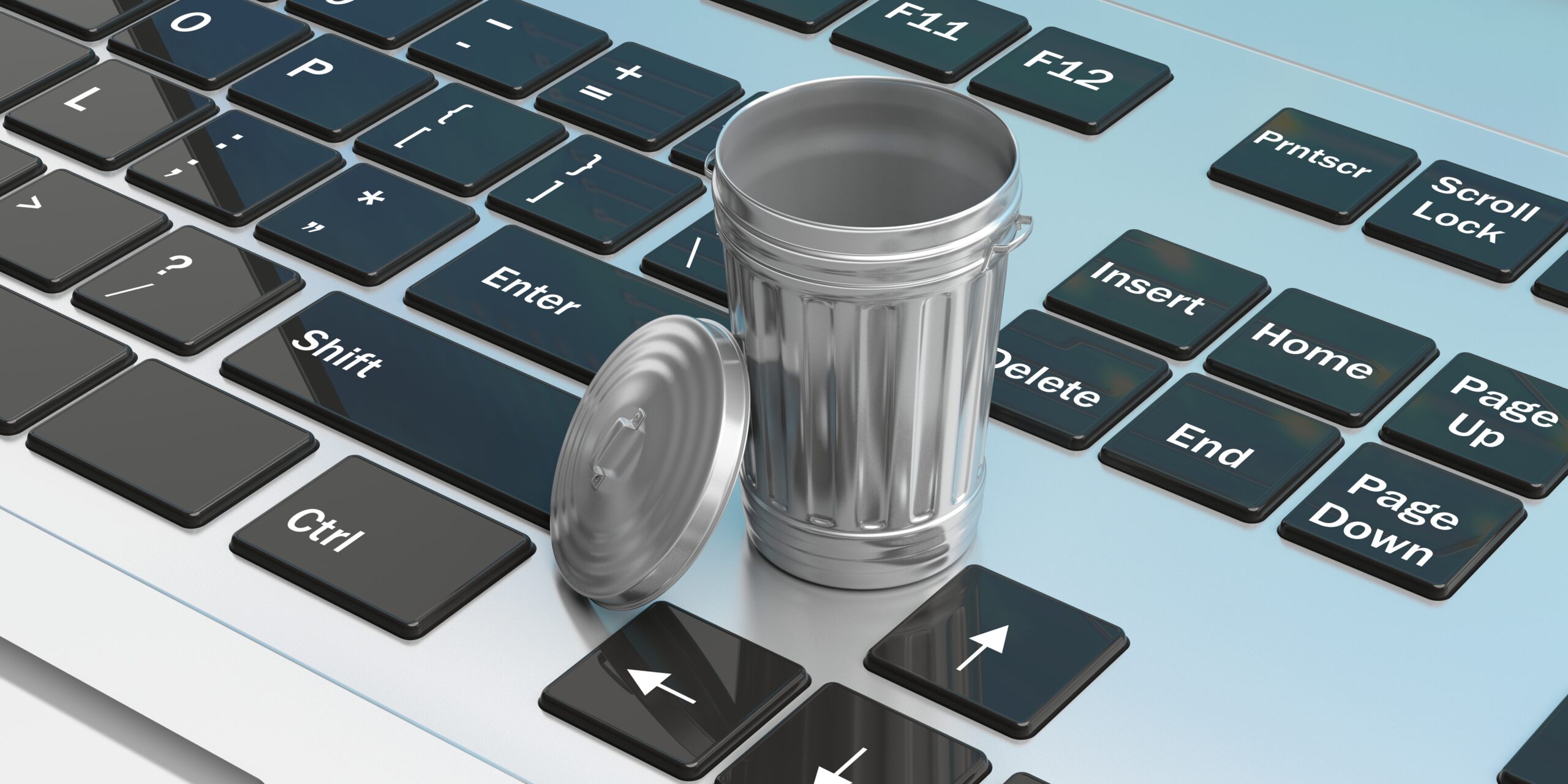 A silver trash can with its lid off is placed on a computer keyboard. The trash can is sitting on the "Shift" key, and the lid is on the "Ctrl" key. Other keys like "Enter," "Delete," and arrow keys are also visible surrounding the trash can.