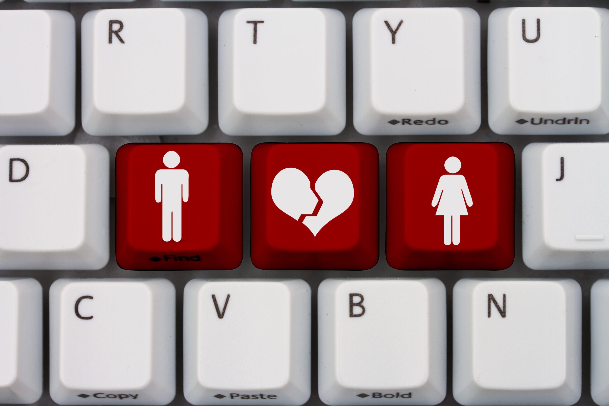 A keyboard with red keys featuring white icons: a male figure on the left key, a broken heart in the middle, and a female figure on the right. The keys are surrounded by standard white keys.