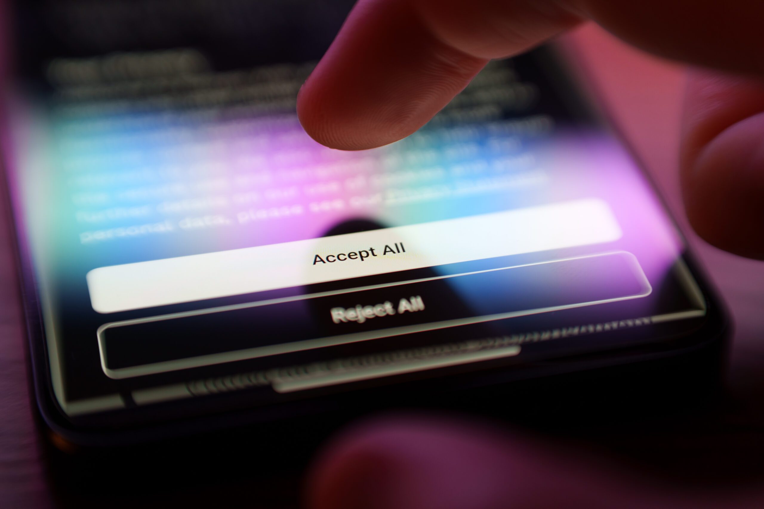 Close-up of a finger about to tap the "Accept All" button on a smartphone screen. The image shows options for accepting terms or settings in an app or website, with a blurred background and soft, colorful lighting.