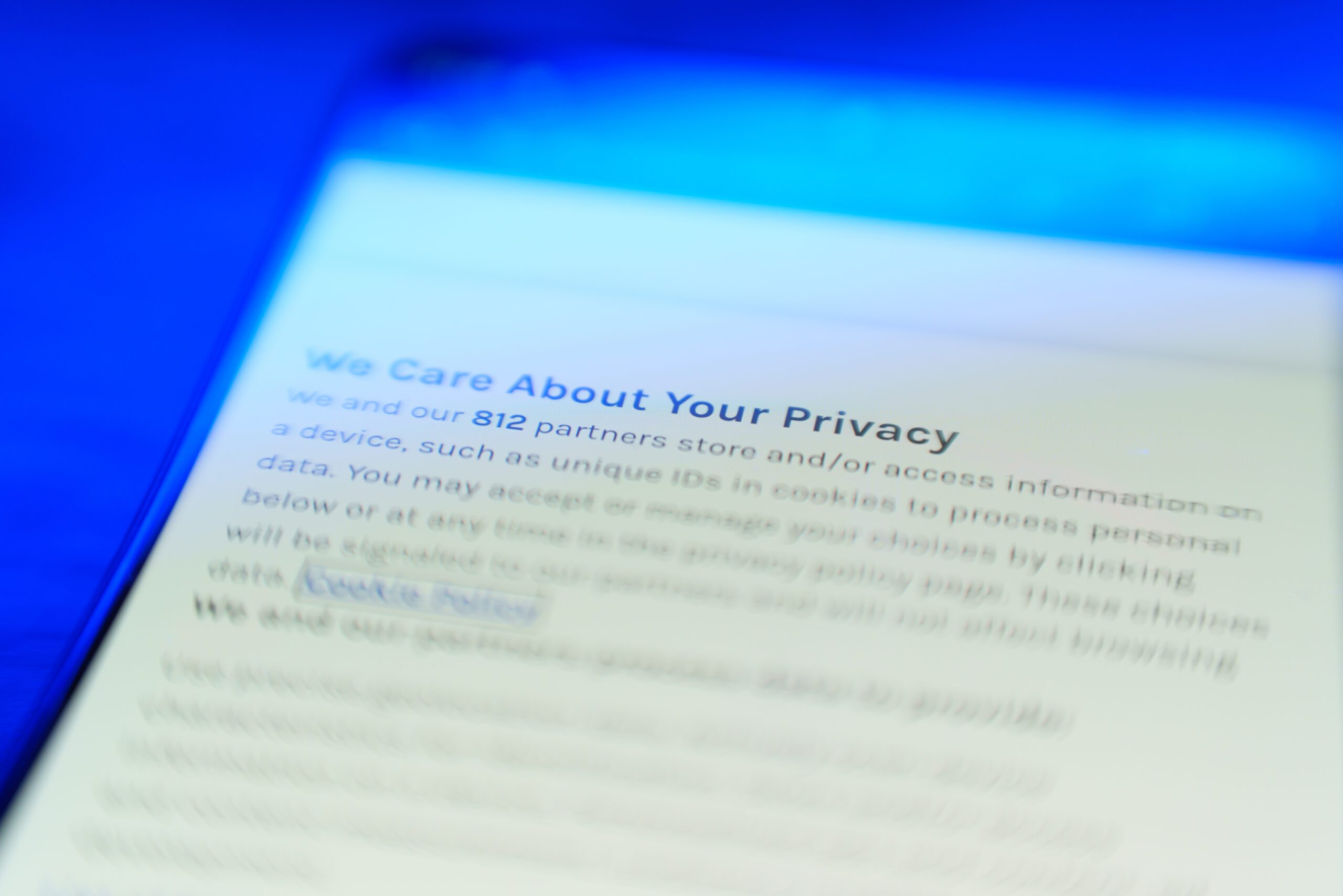 A close-up of a smartphone screen displaying a blurred privacy notice about data and cookie usage, with the heading "We Care About Your Privacy" in focus under blue lighting.