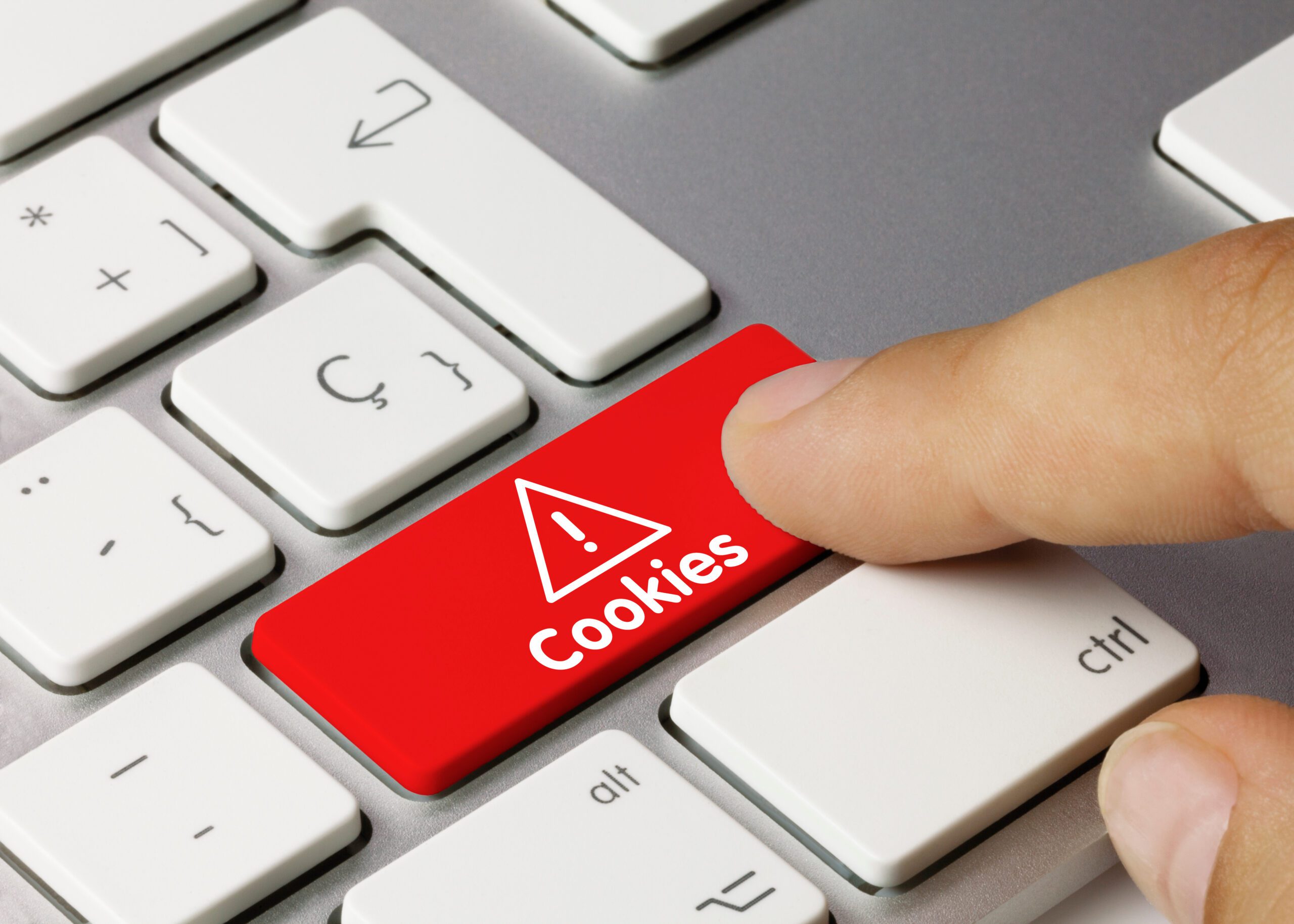 A finger pressing a bright red keyboard key labeled "Cookies" with a warning symbol, surrounded by standard white keys on a computer keyboard.