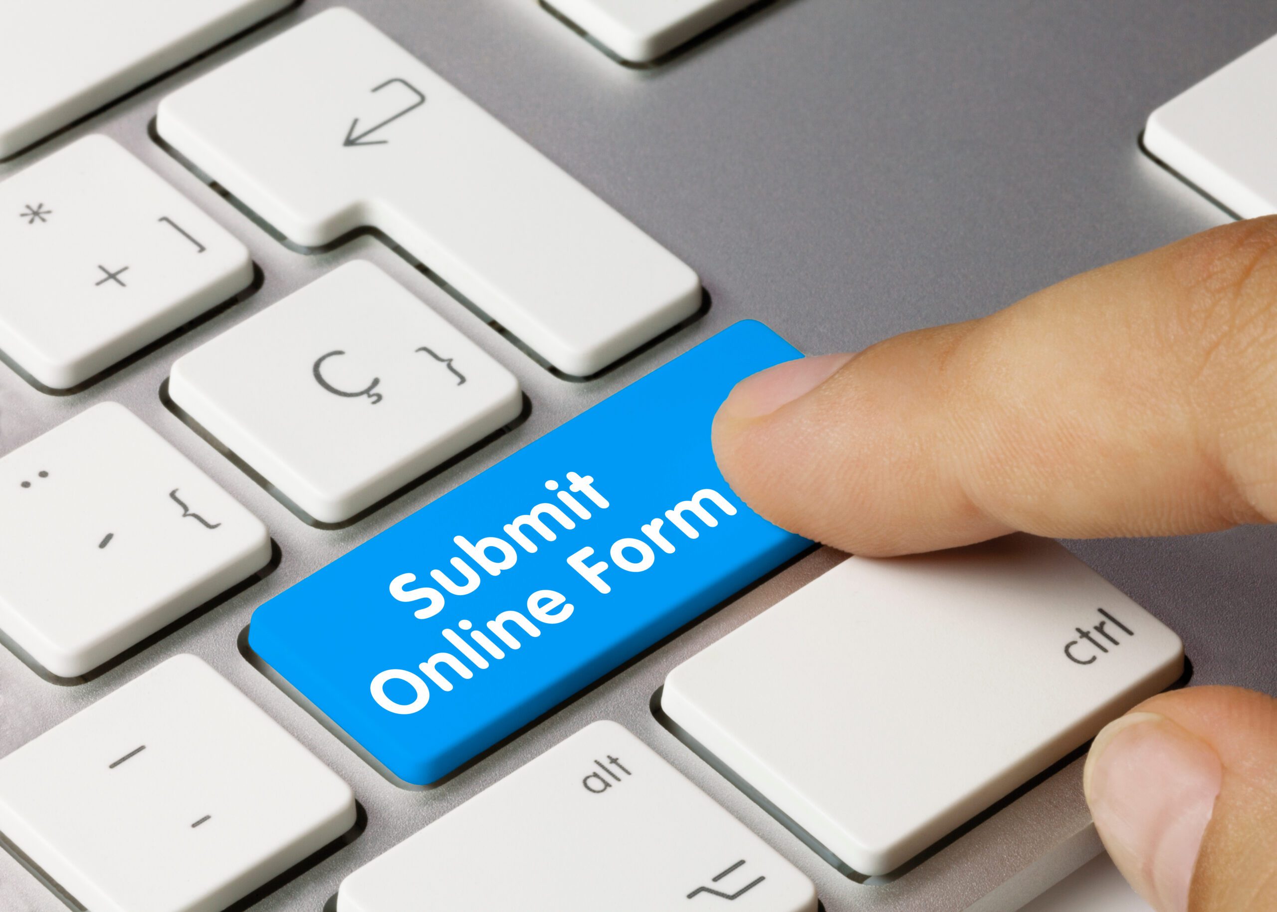 A close-up of a hand pressing a bright blue keyboard key labeled “Submit Online Form” on a white computer keyboard.